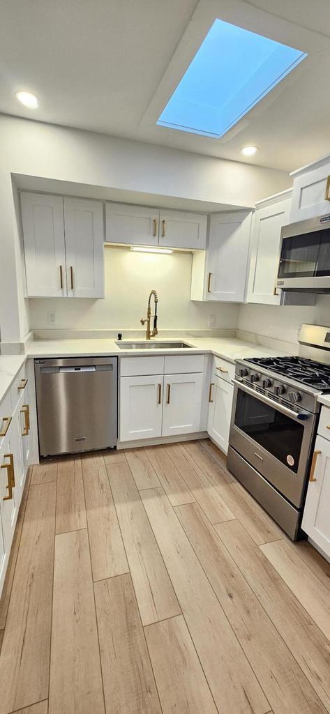 kitchen featuring a skylight, stainless steel appliances, light wood-style floors, and a sink