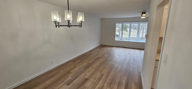 unfurnished dining area featuring hardwood / wood-style flooring, ceiling fan with notable chandelier, baseboards, and visible vents