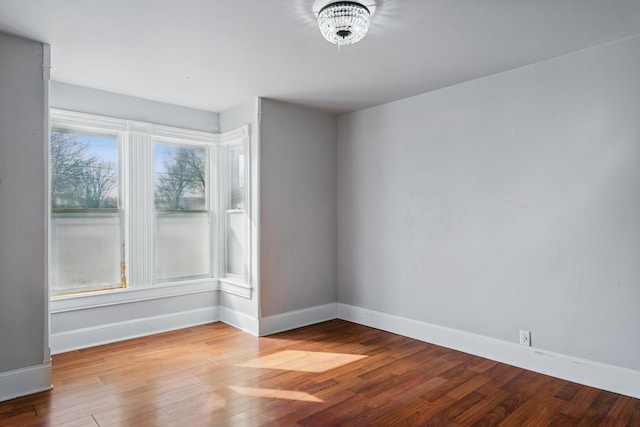 unfurnished room with baseboards, a notable chandelier, and wood finished floors