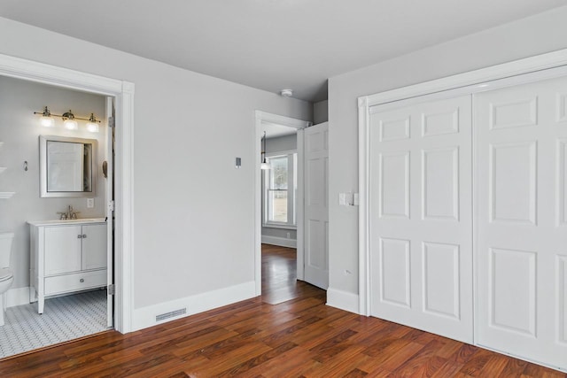 unfurnished bedroom featuring visible vents, connected bathroom, baseboards, dark wood-style floors, and a sink