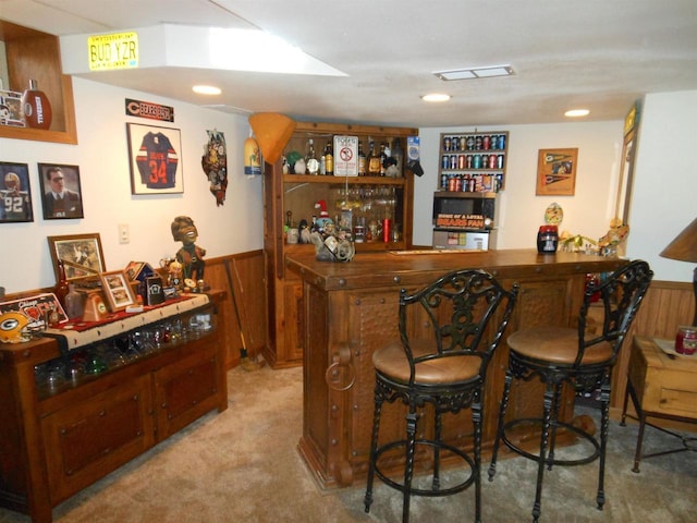 bar with light colored carpet, wooden walls, a bar, and wainscoting