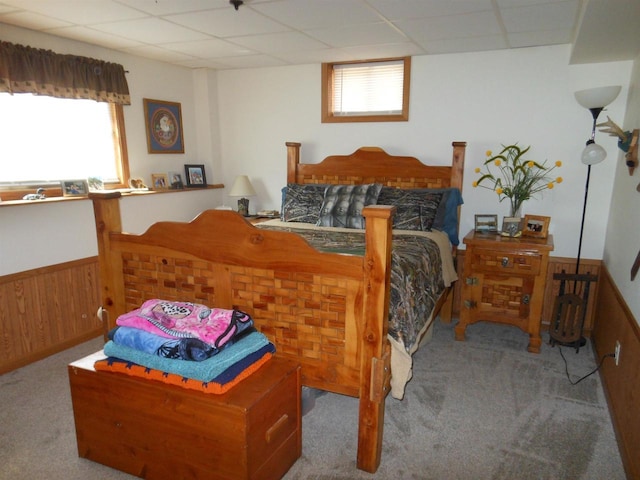 carpeted bedroom with wooden walls, wainscoting, and a drop ceiling