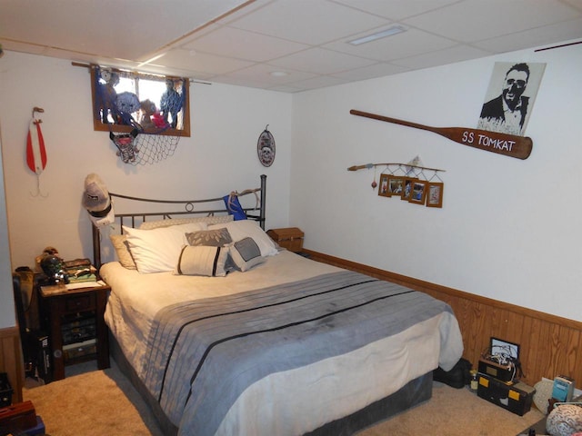 carpeted bedroom with wooden walls, a paneled ceiling, and a wainscoted wall