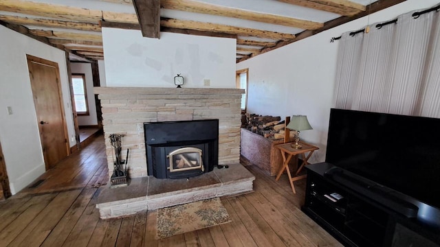 living area with visible vents, beam ceiling, hardwood / wood-style flooring, a stone fireplace, and baseboards