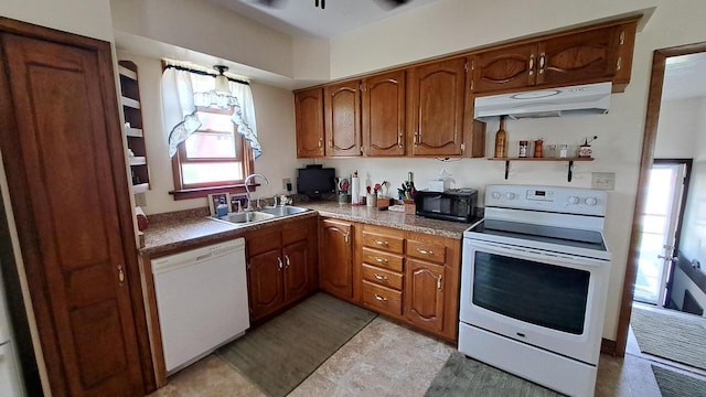 kitchen with under cabinet range hood, white appliances, brown cabinetry, and a sink