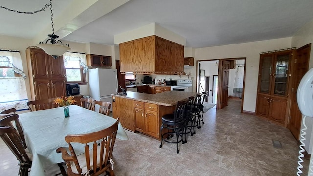 kitchen with brown cabinetry, a breakfast bar, freestanding refrigerator, and electric stove