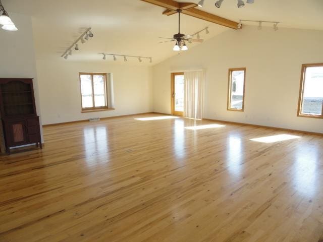 unfurnished living room featuring rail lighting, lofted ceiling with beams, a ceiling fan, and wood finished floors