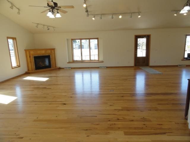 unfurnished living room featuring a glass covered fireplace, rail lighting, light wood-type flooring, and ceiling fan