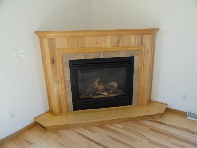 room details featuring visible vents, baseboards, a glass covered fireplace, and wood finished floors