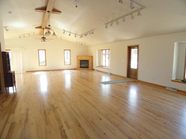 unfurnished living room featuring vaulted ceiling with beams, baseboards, wood finished floors, a glass covered fireplace, and a ceiling fan