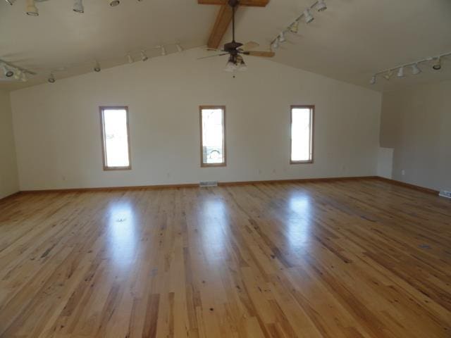 unfurnished room featuring a ceiling fan, lofted ceiling with beams, wood finished floors, rail lighting, and baseboards