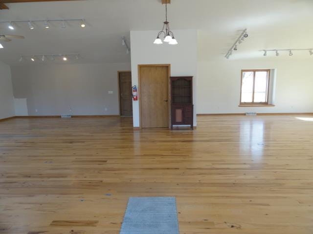 empty room with a notable chandelier, light wood-style flooring, and track lighting