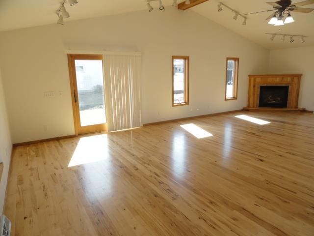 unfurnished living room with track lighting, vaulted ceiling with beams, wood finished floors, and a fireplace with raised hearth