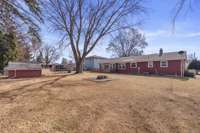 rear view of property featuring fence, an outdoor fire pit, a storage shed, an outdoor structure, and a chimney