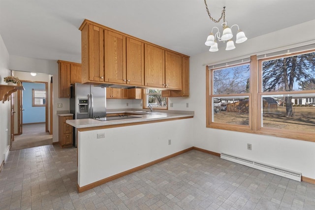 kitchen with brown cabinetry, a peninsula, light countertops, a baseboard heating unit, and stainless steel fridge