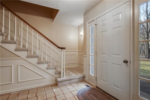 entryway with stairs, wainscoting, tile patterned flooring, and a decorative wall