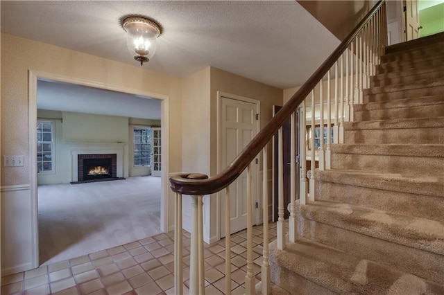 staircase featuring a fireplace, a textured ceiling, and carpet