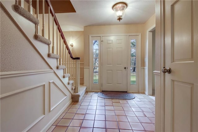 foyer entrance featuring light tile patterned flooring, a wainscoted wall, wallpapered walls, and stairs