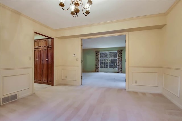 spare room featuring visible vents, a decorative wall, an inviting chandelier, and ornamental molding