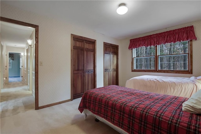 bedroom with light carpet, two closets, wallpapered walls, and baseboards