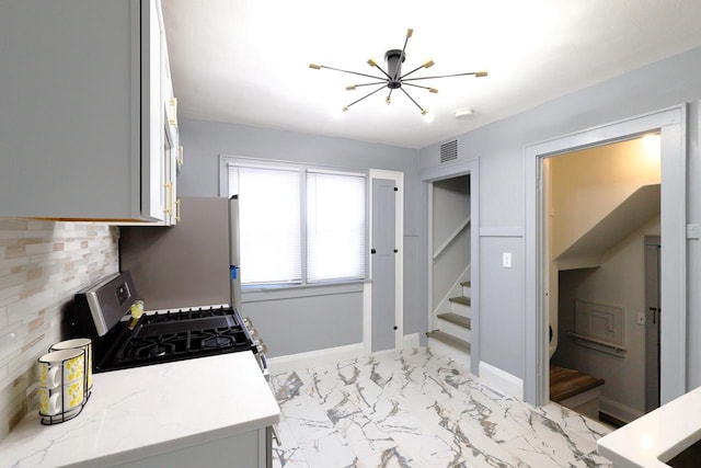 kitchen featuring visible vents, stainless steel range with gas cooktop, freestanding refrigerator, an inviting chandelier, and marble finish floor