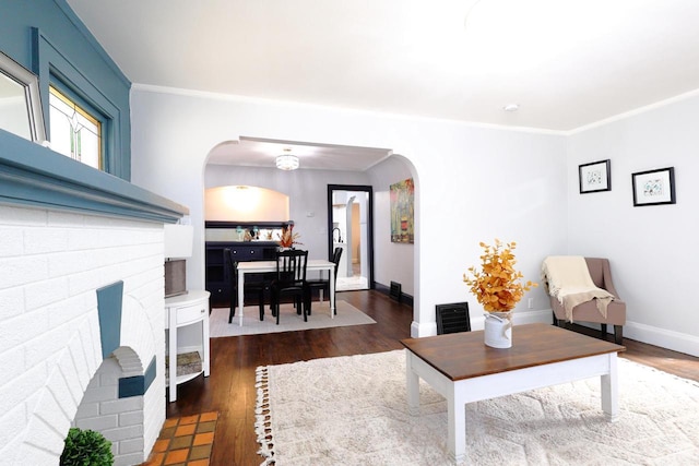 living room featuring dark wood finished floors, crown molding, baseboards, and arched walkways