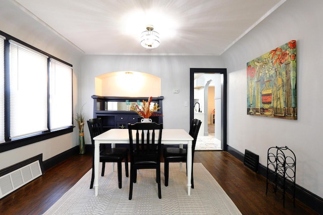 dining room featuring wood finished floors, visible vents, baseboards, arched walkways, and ornamental molding