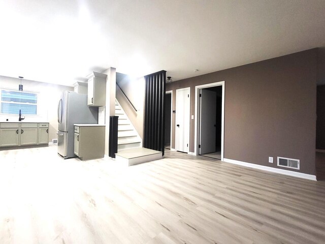 unfurnished living room featuring visible vents, baseboards, light wood-style floors, and stairs