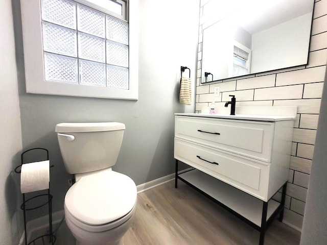 half bathroom featuring tasteful backsplash, wood finished floors, vanity, and toilet