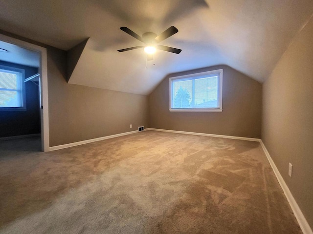 additional living space featuring visible vents, lofted ceiling, carpet flooring, baseboards, and ceiling fan