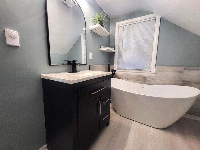 full bath featuring a soaking tub, vanity, and vaulted ceiling