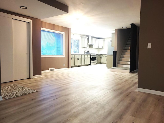 unfurnished living room with light wood finished floors, visible vents, stairs, and baseboards