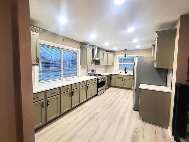 kitchen featuring light wood finished floors, appliances with stainless steel finishes, gray cabinetry, and wall chimney range hood