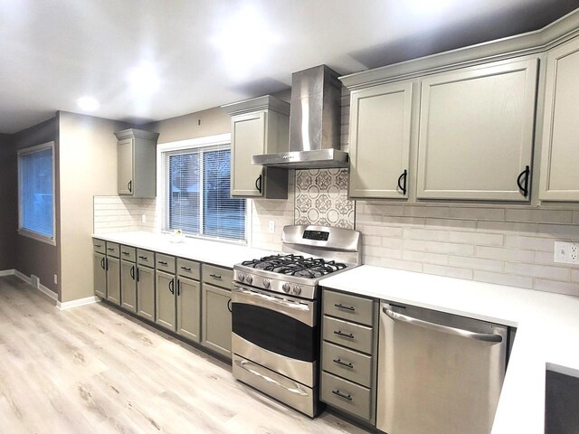 kitchen with gray cabinetry, light countertops, appliances with stainless steel finishes, light wood-style floors, and wall chimney exhaust hood