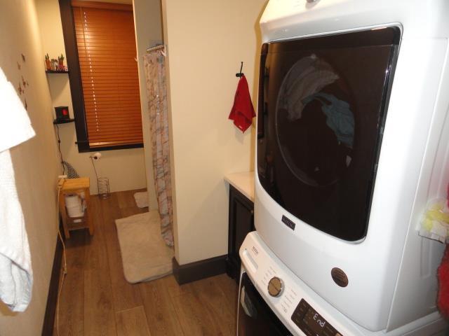 laundry room with laundry area, wood finished floors, stacked washer and clothes dryer, and baseboards