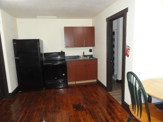 kitchen with dark countertops, baseboards, dark wood-style floors, black appliances, and a sink