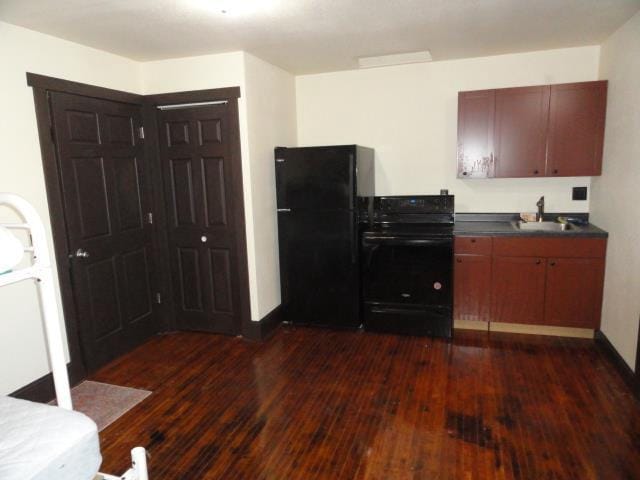 kitchen with baseboards, dark wood finished floors, a sink, black appliances, and dark countertops