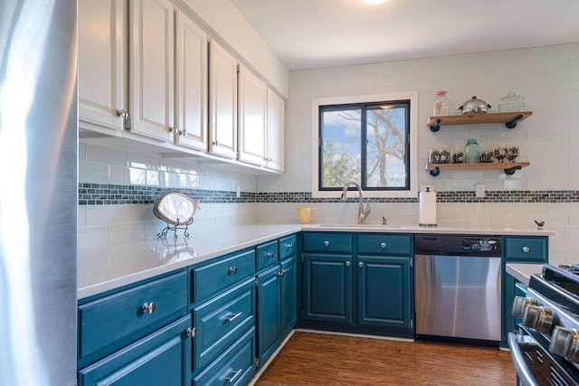 kitchen featuring dark wood-type flooring, blue cabinetry, a sink, appliances with stainless steel finishes, and decorative backsplash