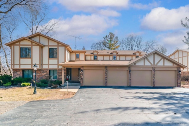 english style home featuring a chimney, stucco siding, a garage, aphalt driveway, and brick siding