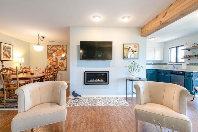 living room featuring a glass covered fireplace, baseboards, beam ceiling, and wood finished floors