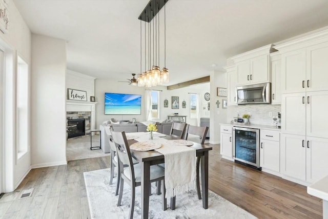 dining space with wine cooler, a ceiling fan, light wood-style flooring, and a fireplace