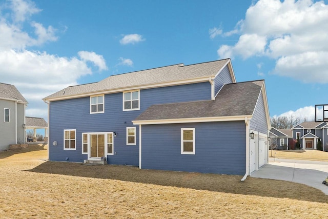 rear view of property featuring a garage, a yard, driveway, and a shingled roof