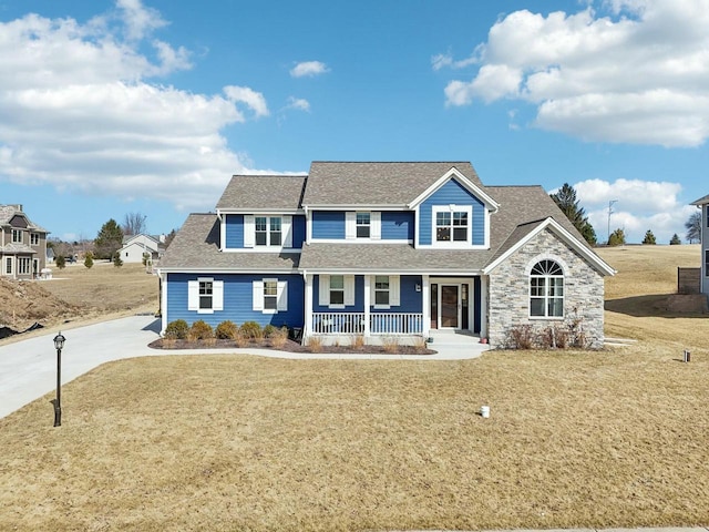 view of front of house with stone siding, a porch, a shingled roof, and a front lawn