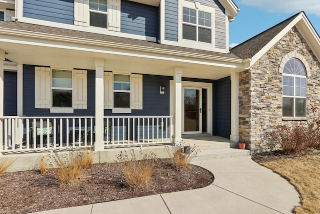 view of exterior entry featuring covered porch, stone siding, and a shingled roof