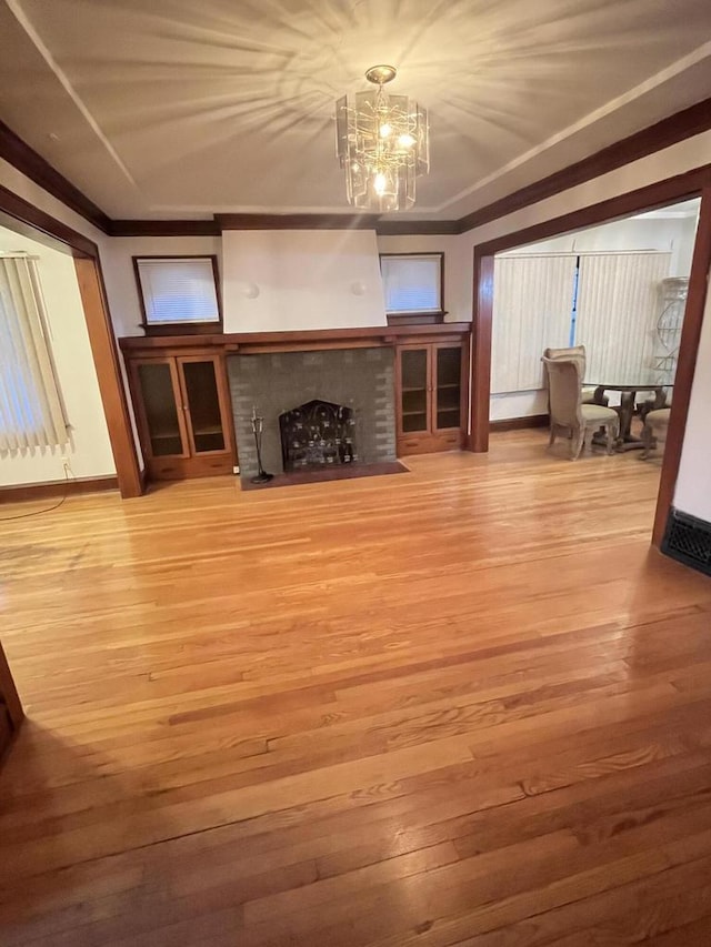 unfurnished living room featuring a fireplace, an inviting chandelier, wood finished floors, and ornamental molding