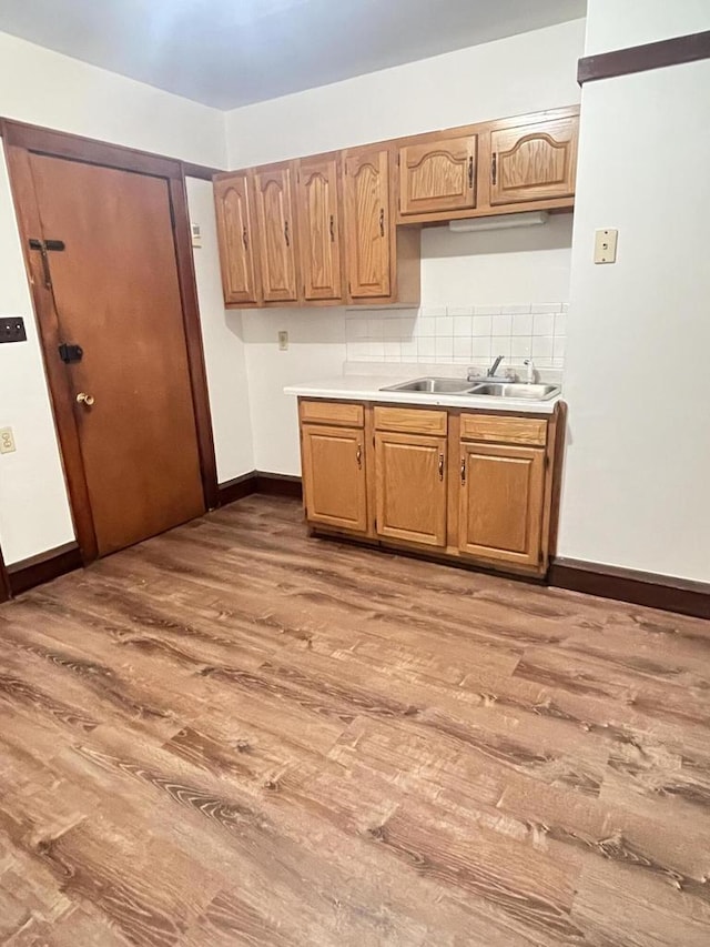 kitchen featuring a sink, tasteful backsplash, wood finished floors, light countertops, and baseboards