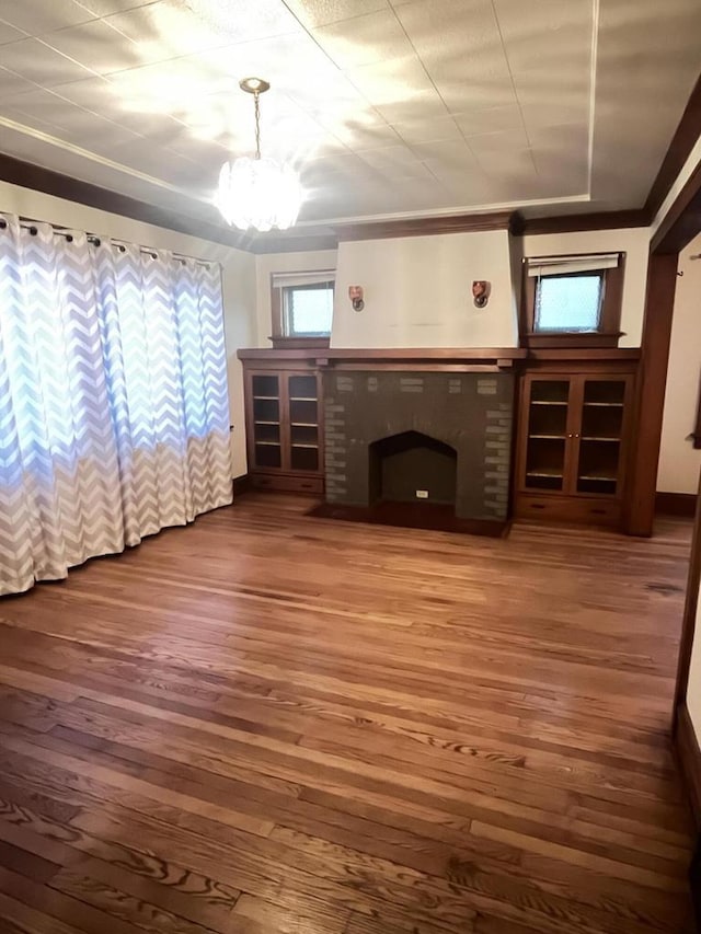 unfurnished living room with a chandelier, a brick fireplace, and wood finished floors