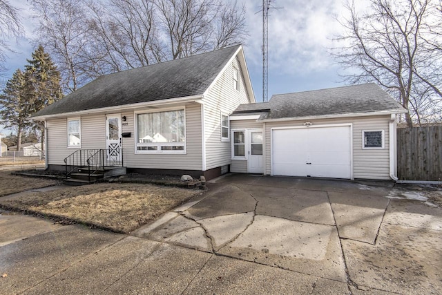 new england style home with a garage, roof with shingles, concrete driveway, and fence