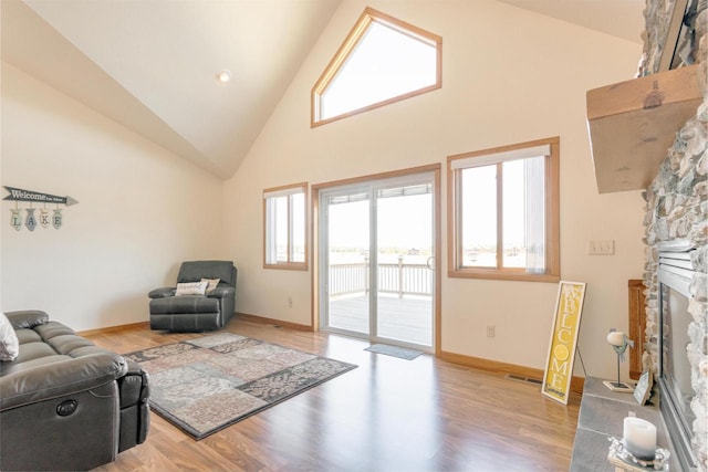 living area with visible vents, high vaulted ceiling, light wood-style floors, a stone fireplace, and baseboards