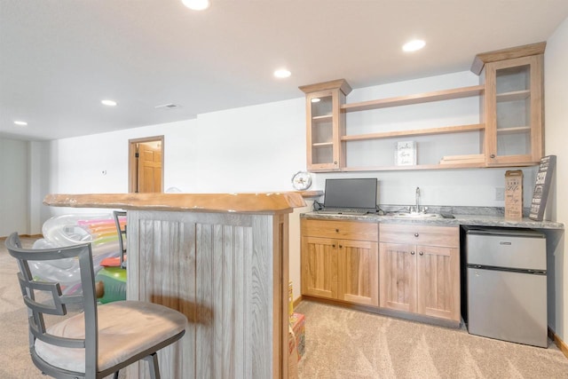 kitchen with open shelves, light brown cabinetry, light carpet, refrigerator, and a sink